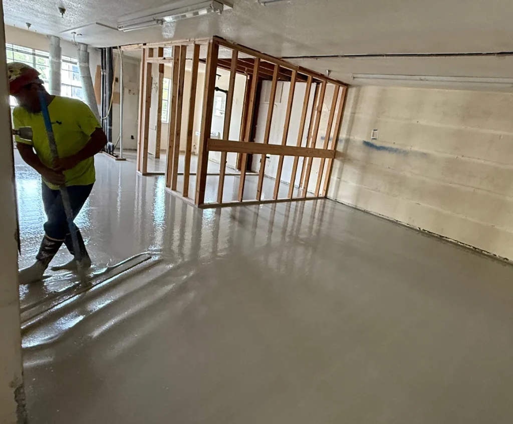 Worker smoothing gypsum concrete underlayment in open interior