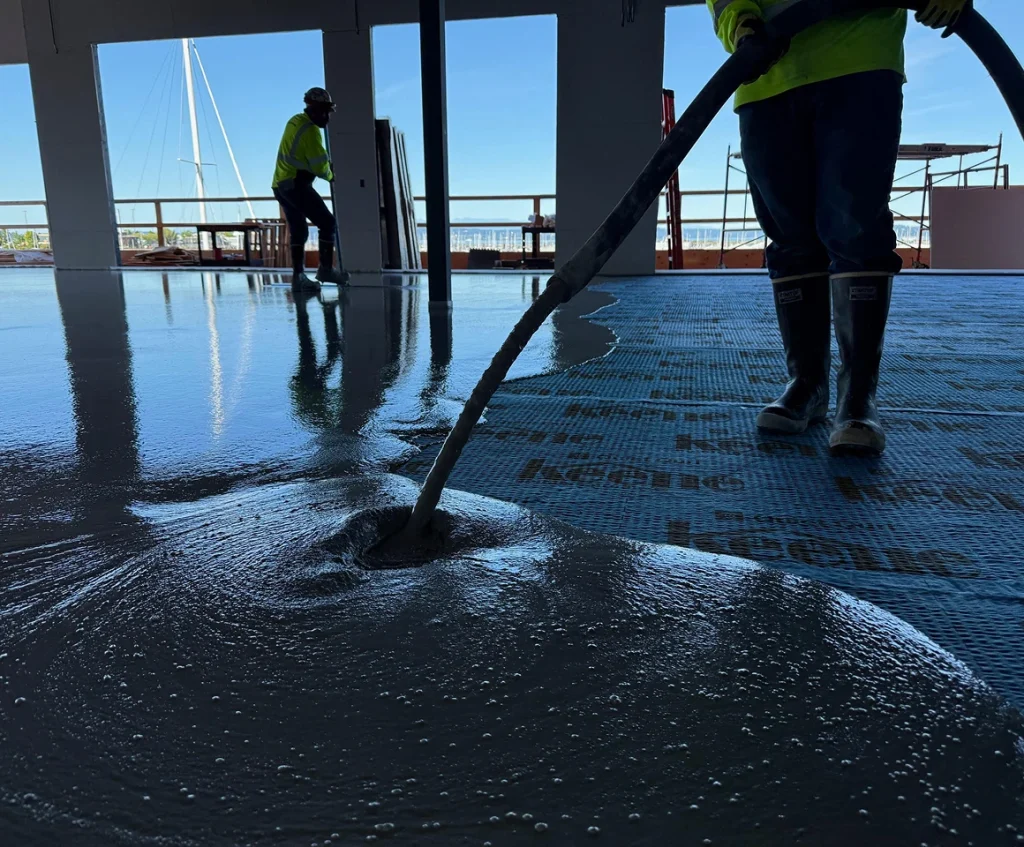 Workers pouring leveling compound over sound control mats on deck